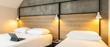 Una habitación de hotel moderna con una cama grande, dos mesitas de noche y una pared de concreto como elemento decorativo.