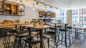 Un café moderno con mesas de madera, sillas negras, una barra de café y ventanas amplias.