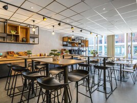 Un café moderno con mesas de madera, sillas negras, una barra de café y ventanas amplias.