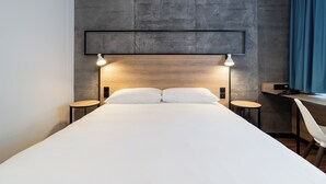 Una habitación de hotel moderna con una cama grande, dos mesitas de noche, un escritorio y una silla.