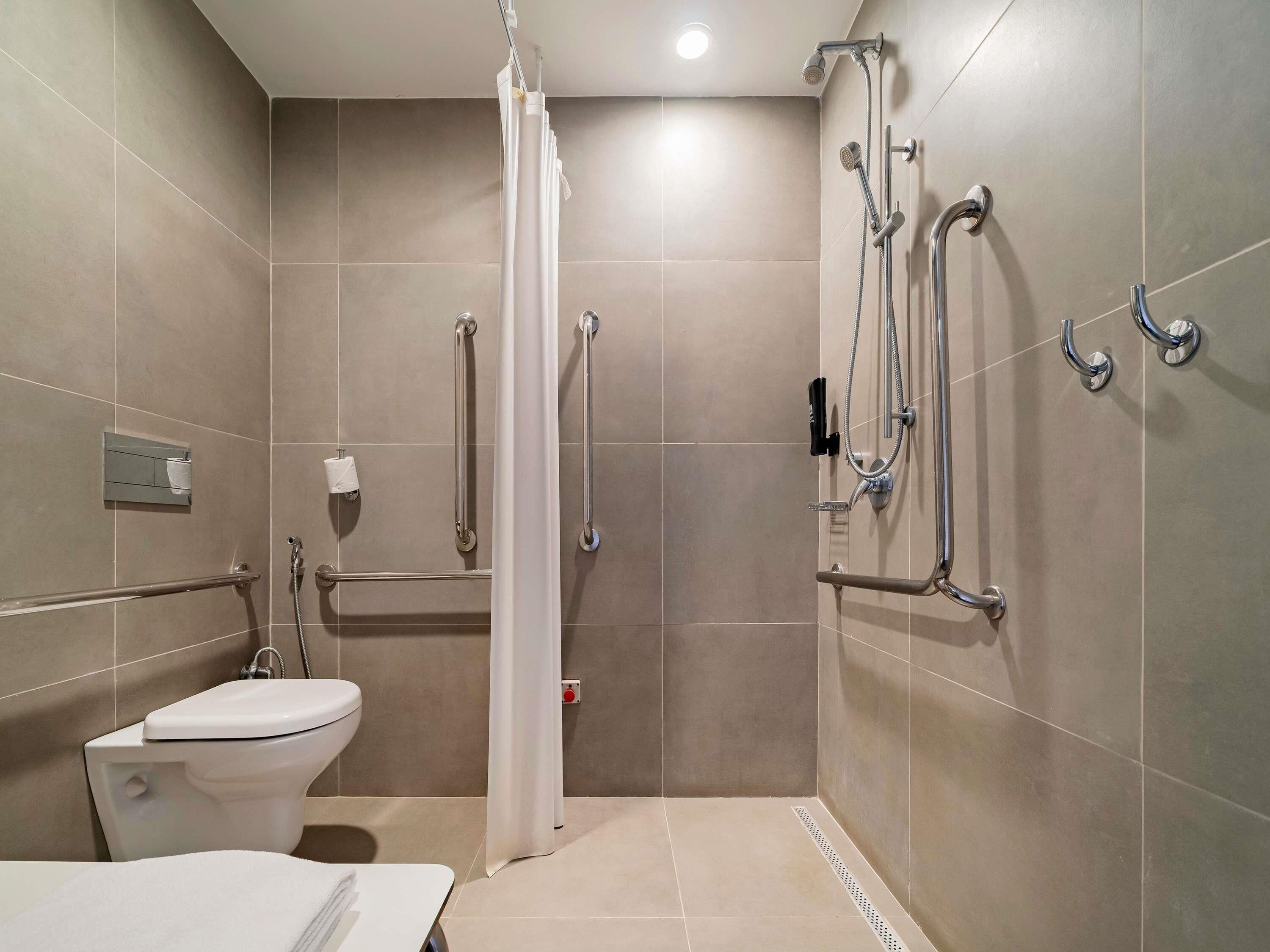 A modern bathroom with a shower, toilet, and grab bars.