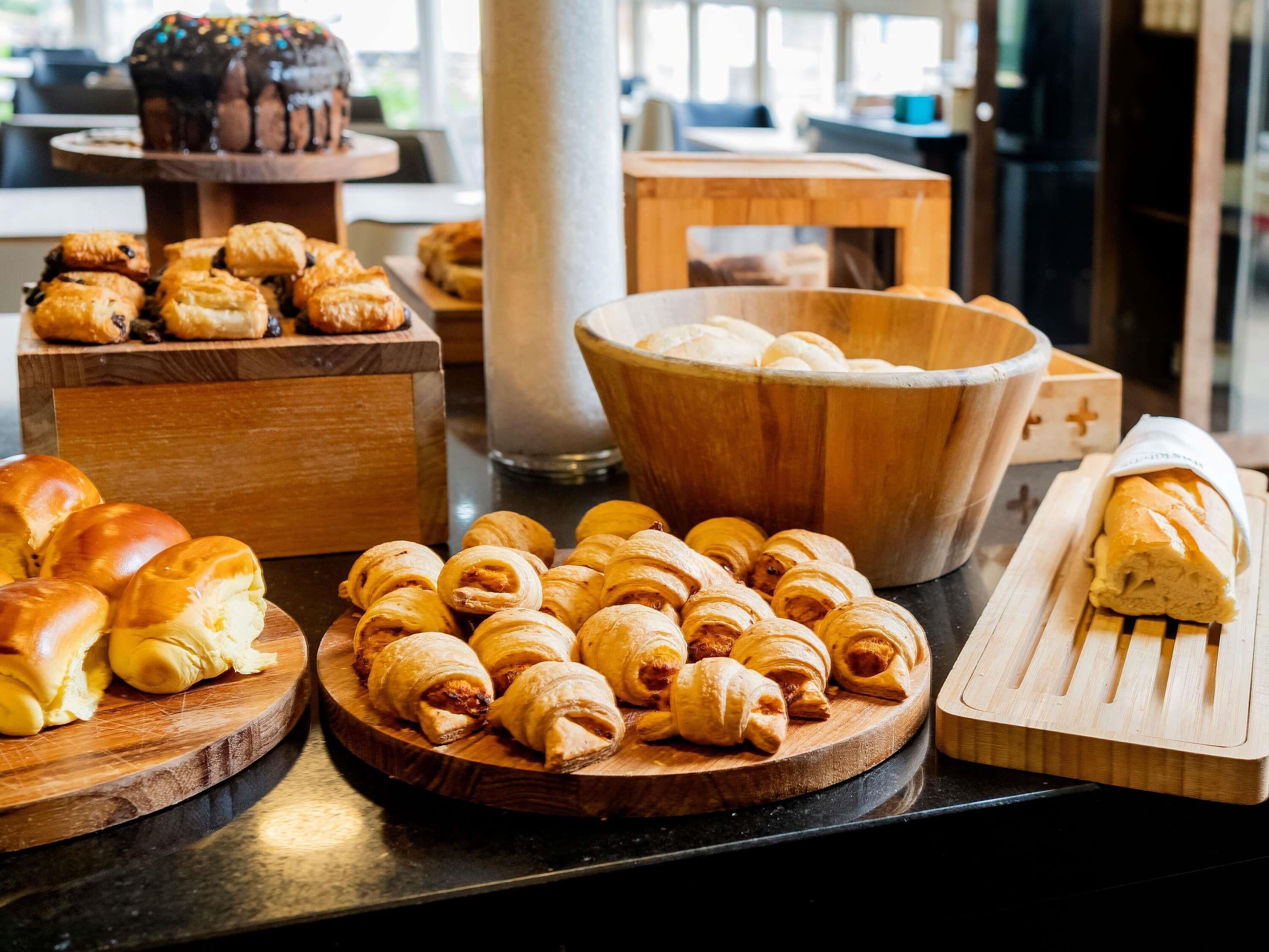 A variety of baked goods displayed on wooden boards, including croissants and bread, in a bakery setting.