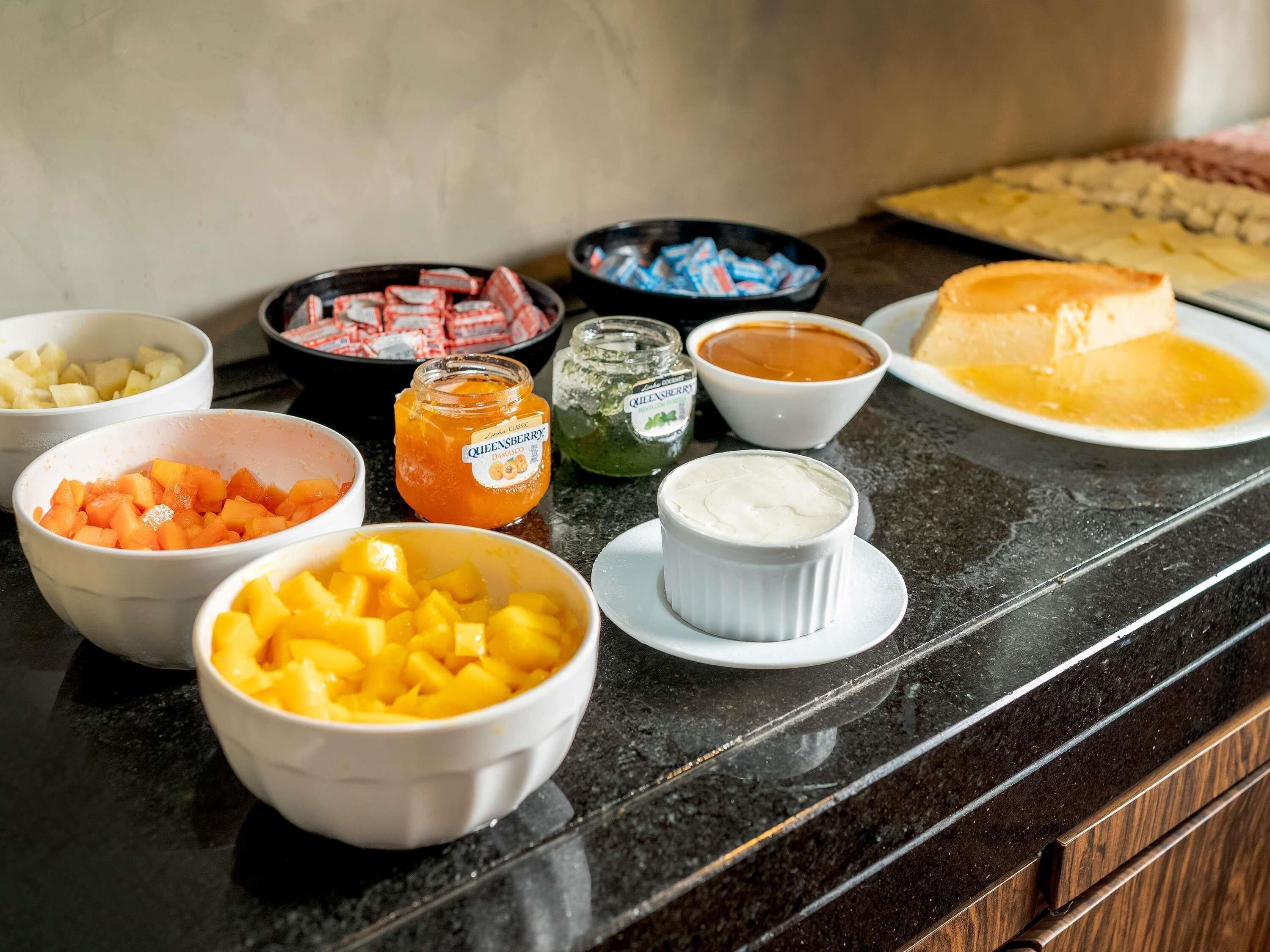 A kitchen counter with various food items and condiments, including bowls of diced fruits, a jar of jam, and a pie.
