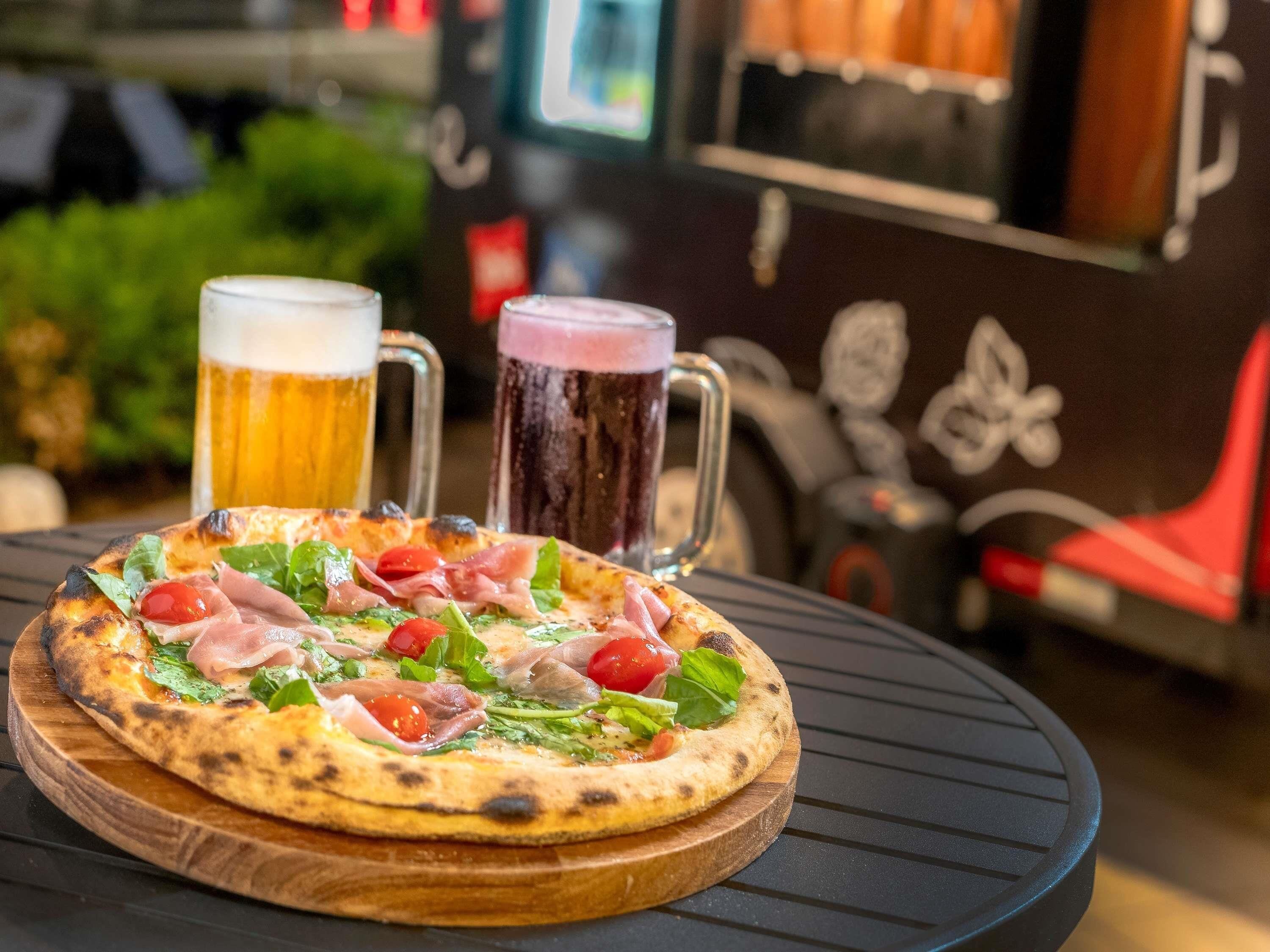 A pizza on a wooden board with two beer mugs in the background.