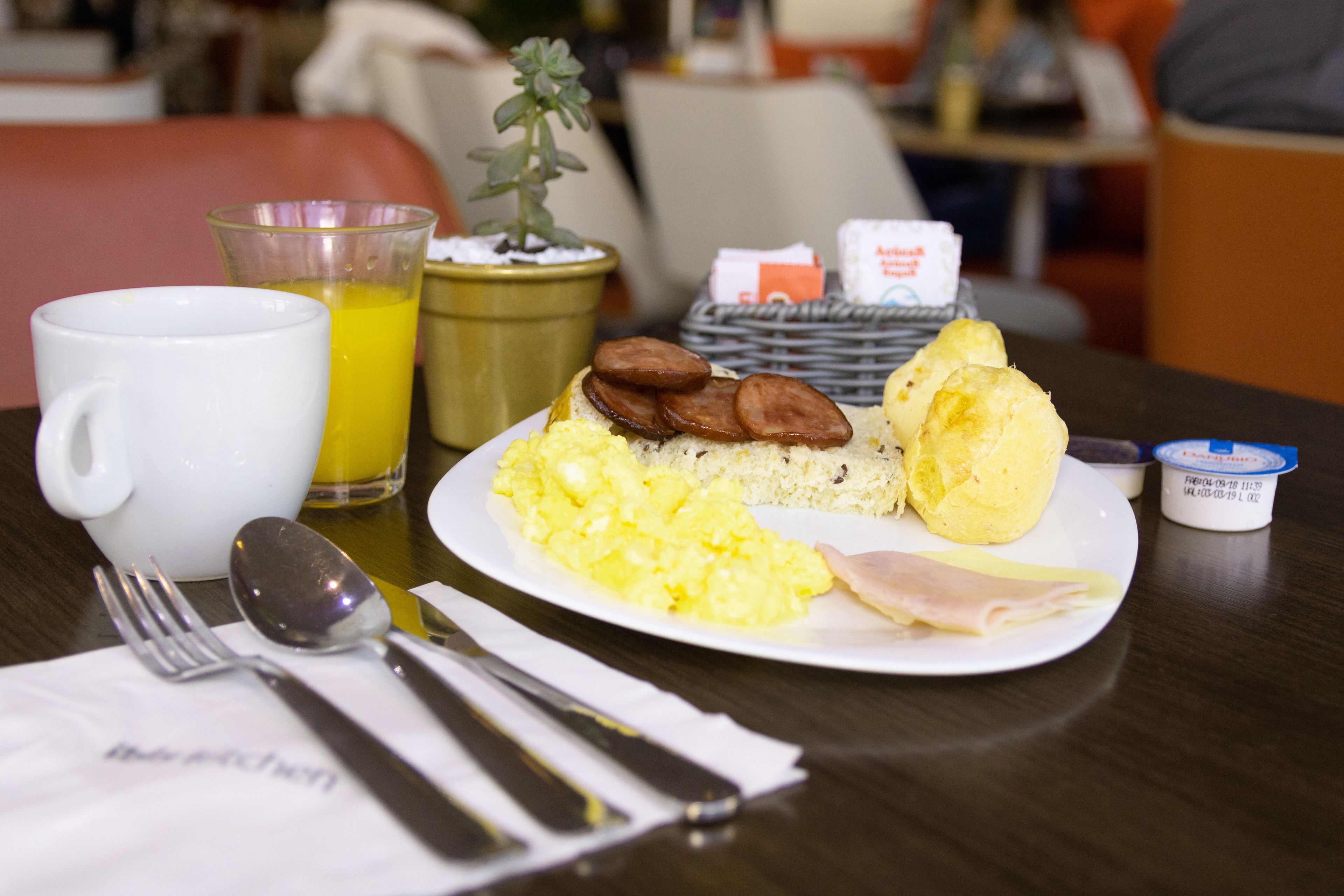 A breakfast plate with scrambled eggs, ham, and a muffin, accompanied by a glass of orange juice and a small plant.