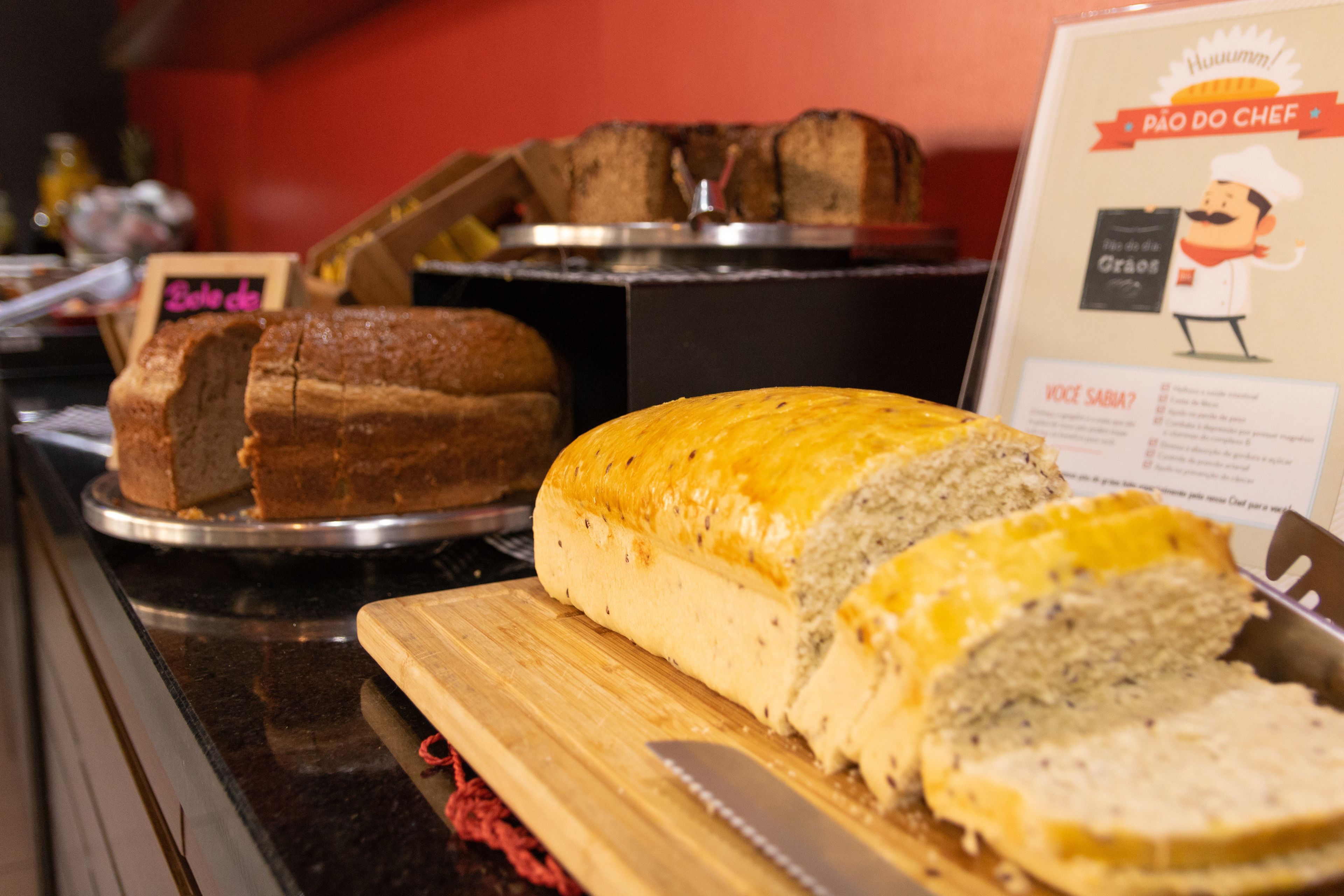 A bakery display with various breads and a sign reading "Pão do Chef".