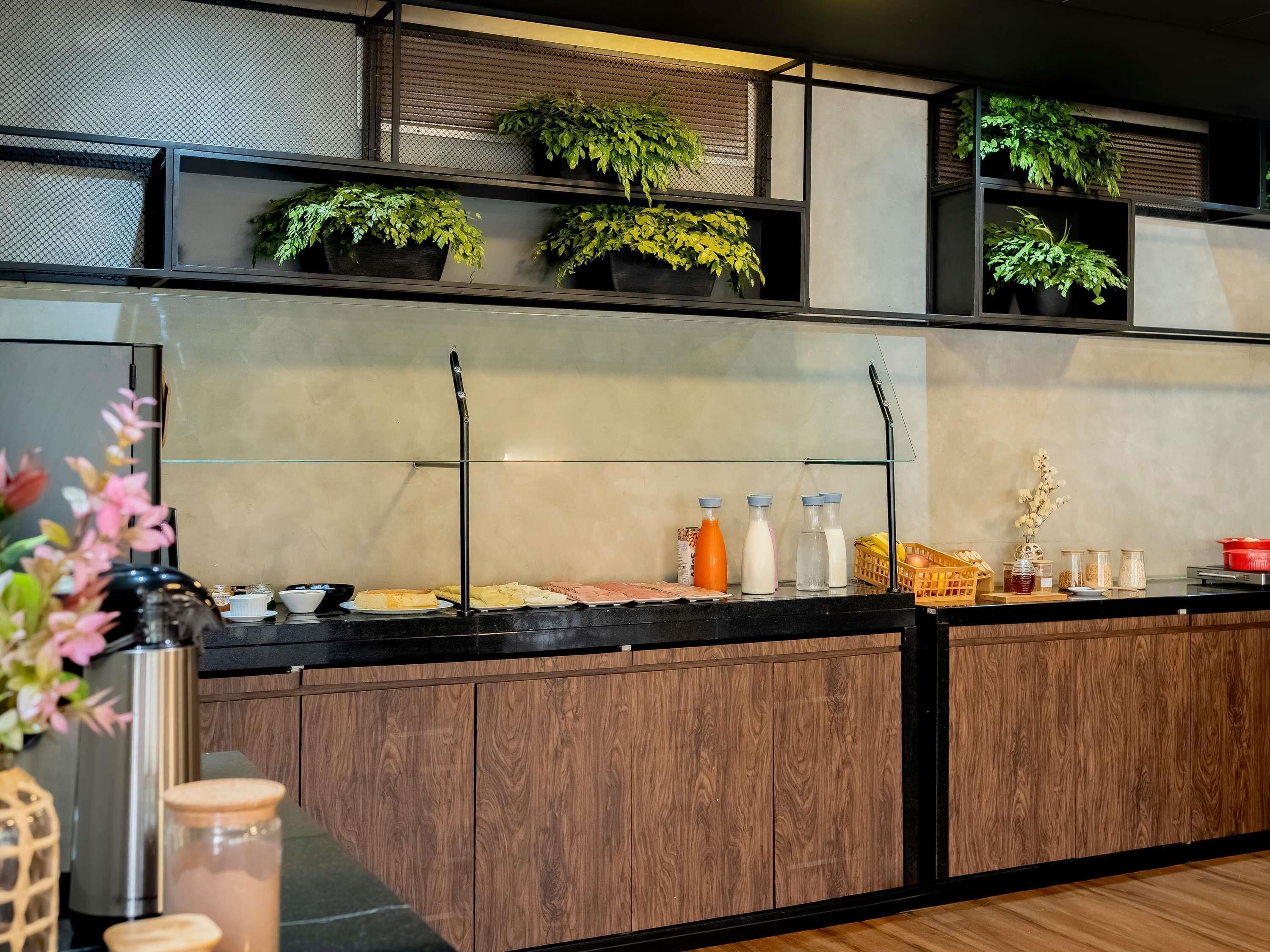A modern kitchen with wooden cabinets, a black countertop, and potted plants on shelves.