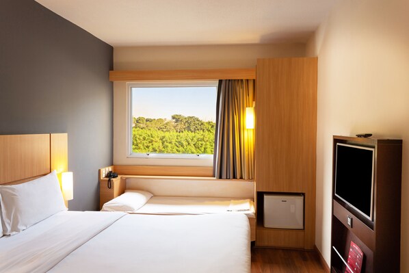 A hotel room with a large bed, a TV, a small fridge, and a window with curtains.