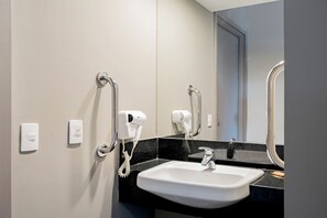 Un baño con lavamanos, dos secadores de pelo y un espejo.