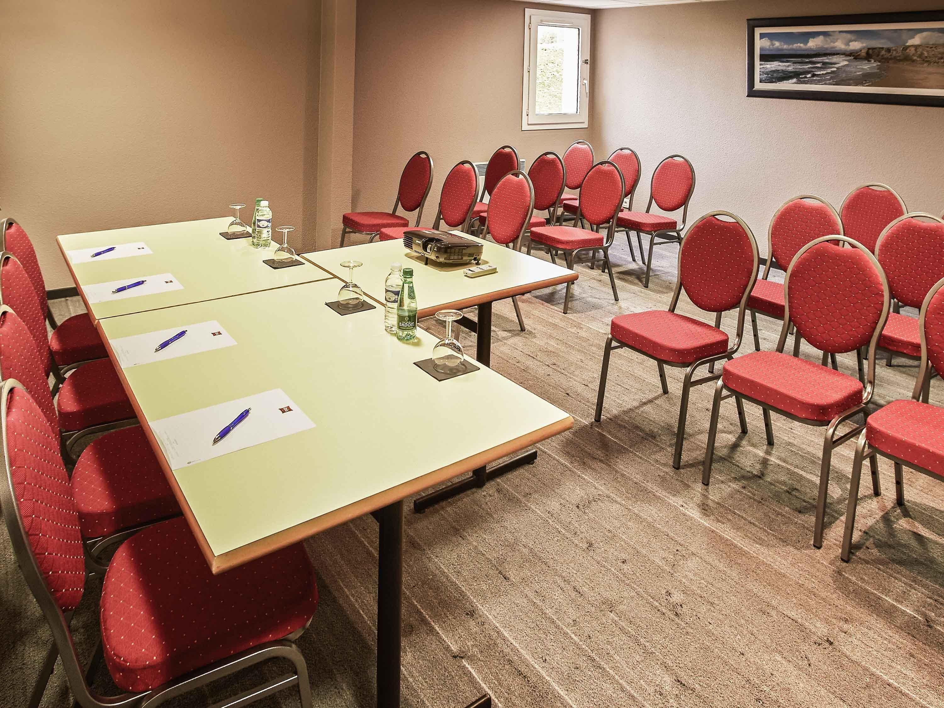 A conference room with a long table, red chairs, water bottles, and documents.