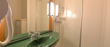 Un baño con un lavamanos verde, un espejo, ducha con cerramiento de vidrio y un inodoro blanco.