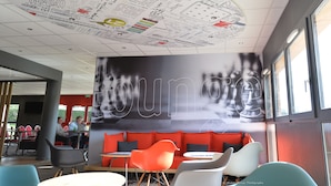A modern interior with a ceiling decorated with sketches and notes, a large wall mural, and a seating area with orange and white chairs. - ibis Auray (Auray)