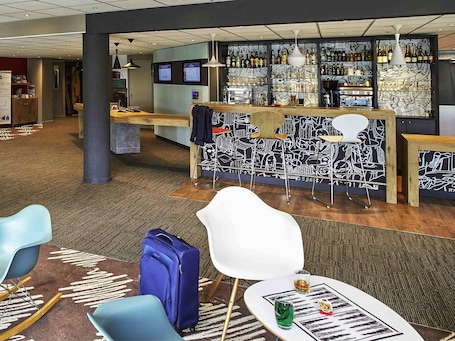 A hotel lobby with a bar area, seating, and a luggage trolley.. ibis Auray