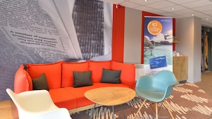A modern lobby with a red sofa, a round wooden table, and a blue chair. - ibis Auray (Auray)