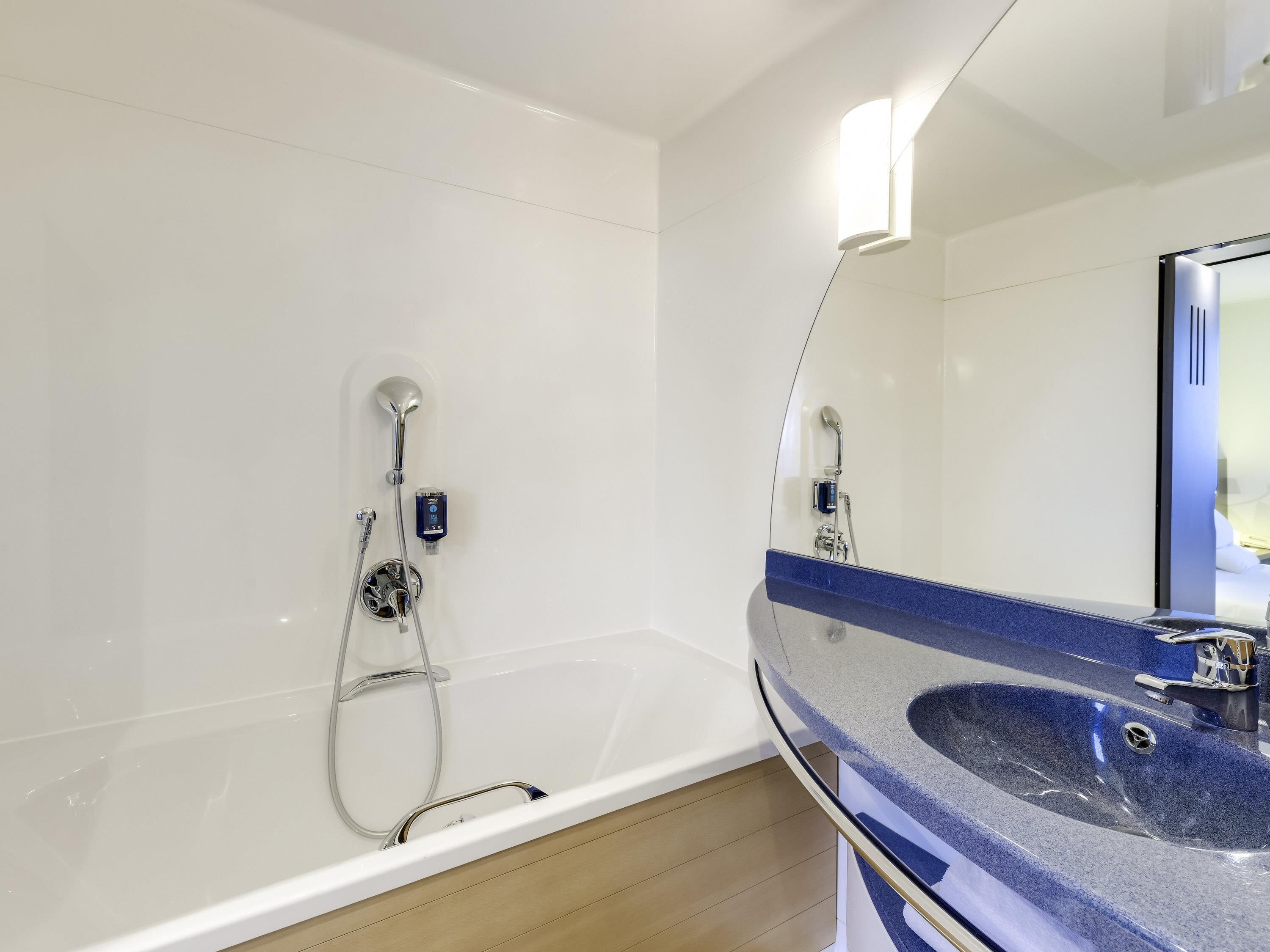 Une salle de bain moderne avec une baignoire blanche, un lavabo bleu et un grand miroir.