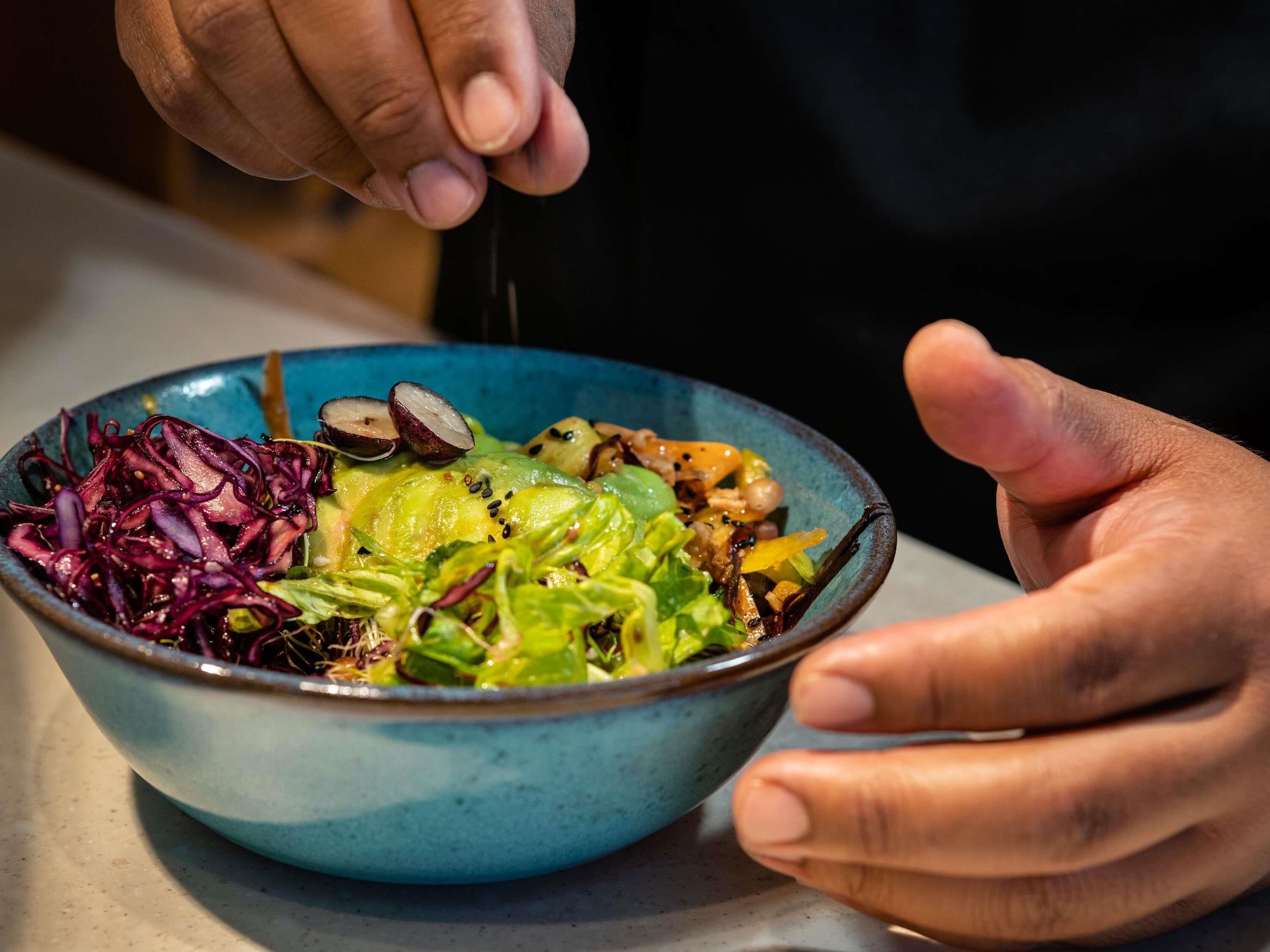 Une personne tenant un saladier rempli d’une salade composée de différents légumes et d’une vinaigrette.