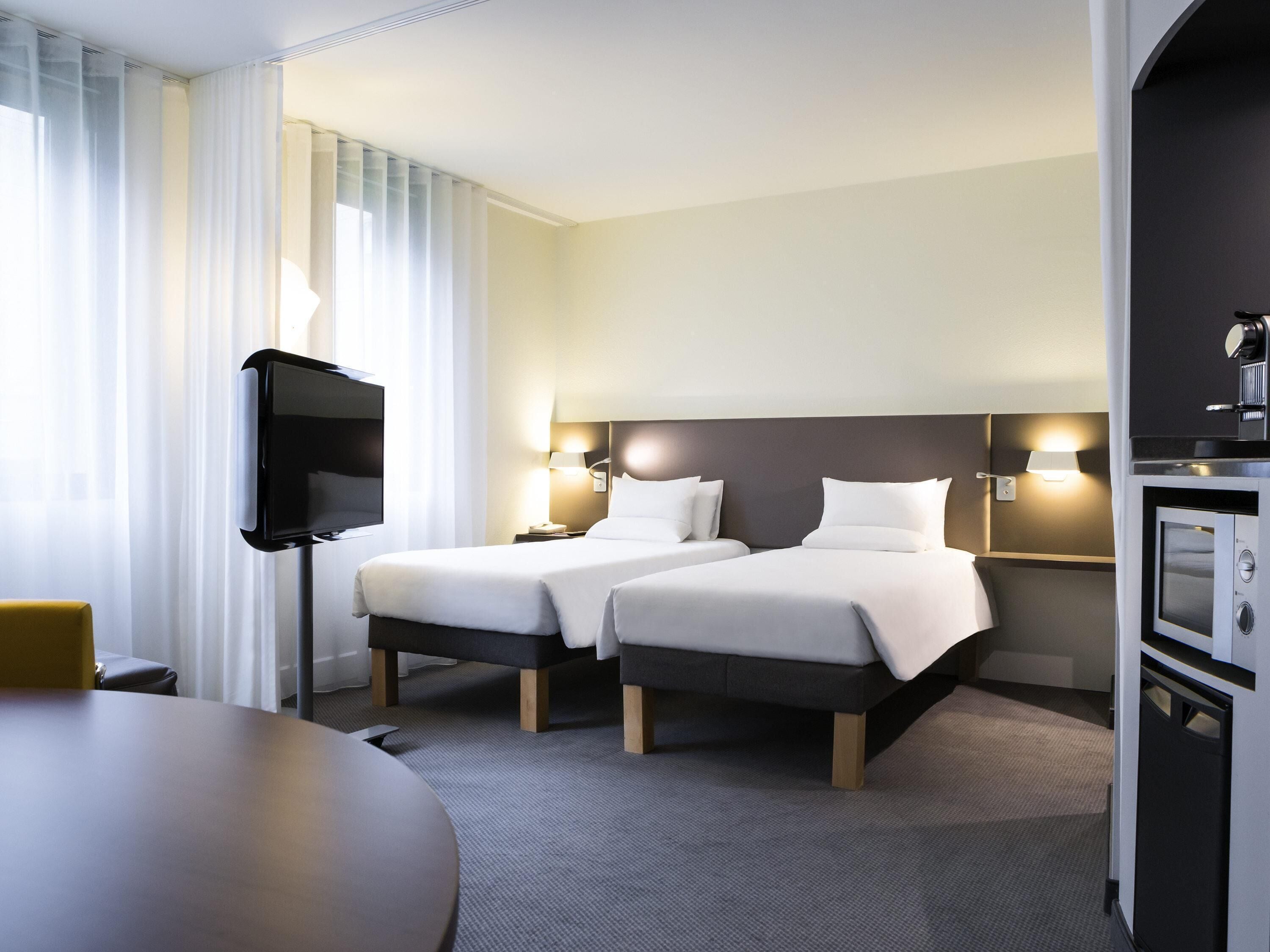 A hotel room with two beds, a TV, a desk, and a minibar.