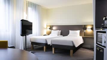A hotel room with two beds, a TV, a desk, and a minibar.