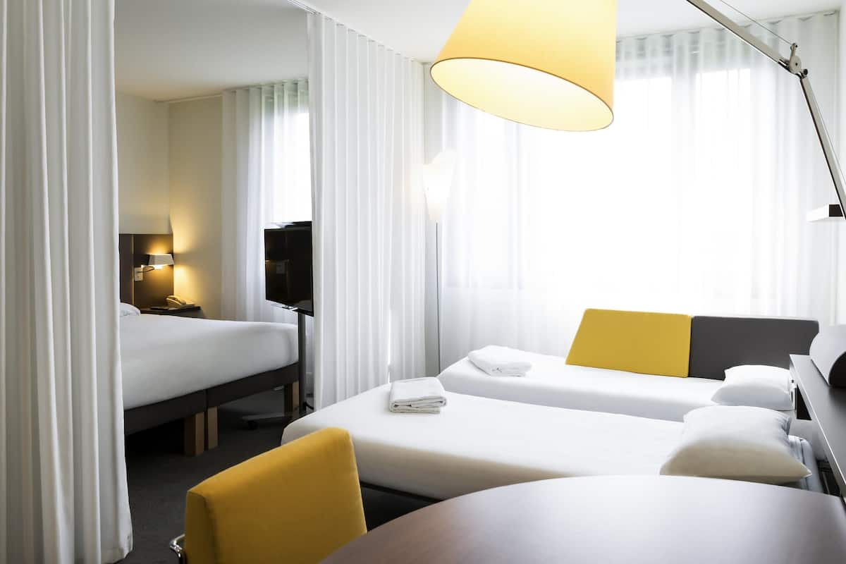 Une chambre d’hôtel avec deux lits, un bureau, une chaise, une télévision et une lampe.