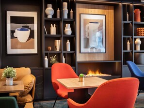 Un interior moderno con chimenea, sillas naranja y azul, y estanterías con diversos objetos decorativos.