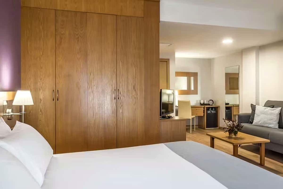 Hotellihuoneessa on sänky, puinen vaatekaappi, työpöytä tuolilla, sohva ja pieni keittiöalue.