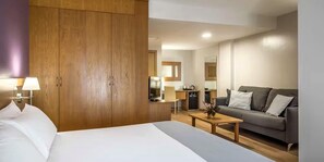 A hotel room with a bed, a wooden wardrobe, a desk with a chair, a sofa, and a small kitchen area. - Hotel RH Jerez Centro (Jerez de la Frontera)