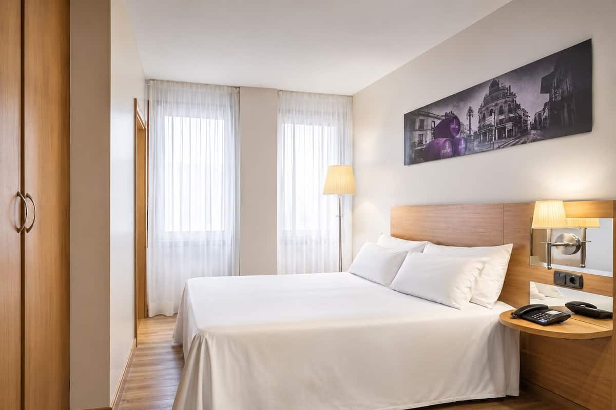 Une chambre d’hôtel avec un lit, une table de chevet, une lampe, un téléphone et un tableau au mur.