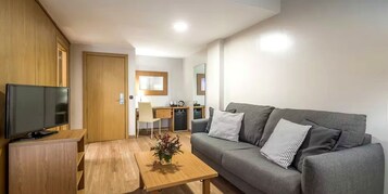 Una sala moderna con un televisor de pantalla plana, un sofá gris con cojines estampados, una mesa de centro de madera y un escritorio con una silla.