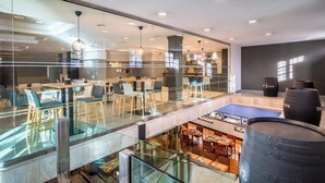 Un vestíbulo de hotel moderno con barandillas de cristal, varias zonas de comedor y una zona de bar visible.