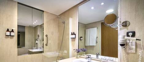 Un baño moderno con un espejo grande, ducha, lavamanos y secador de pelo.