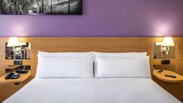 Habitación de hotel con cabecera de madera, ropa de cama blanca, dos mesitas de noche con lámparas, un teléfono y un control remoto.
