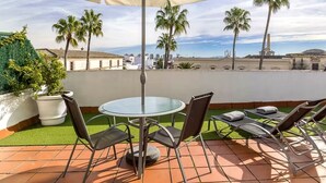 Una terraza con una mesa redonda de vidrio, sillas de metal y tumbonas.