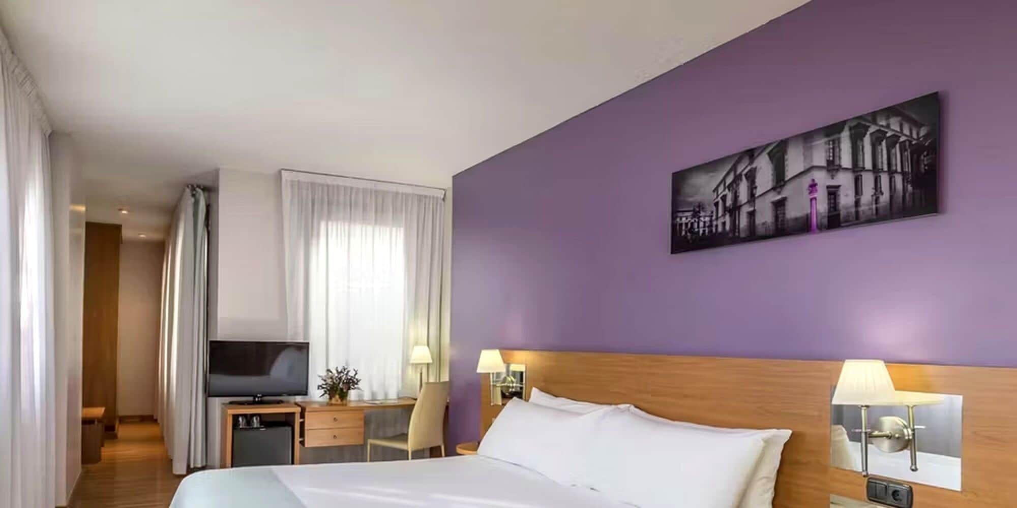 Een hotelkamer met een bed, een televisie, een bureau en een schilderij aan de muur.