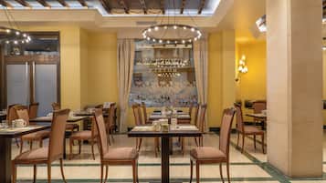 A dining area with multiple tables and chairs, a chandelier, and a mural on the wall.