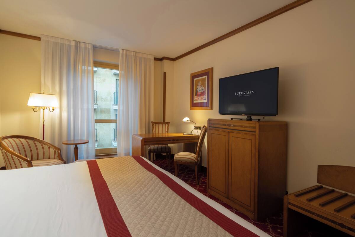 Een hotelkamer met een groot bed, een bureau, een televisie en een stoel.