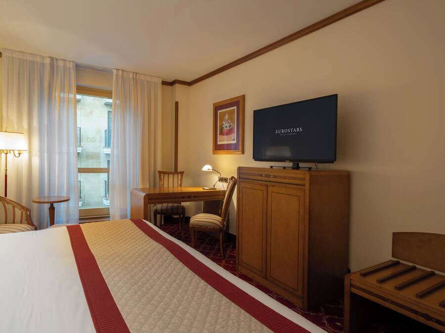 Una habitación de hotel con una cama, un escritorio, un televisor y una silla.