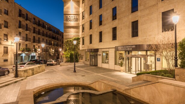 A hotel with a modern facade, a courtyard with a water feature, and a well-lit entrance.