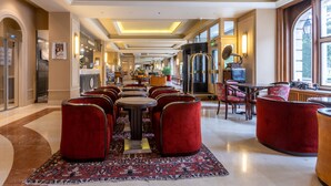 A spacious hotel lobby with a central seating area featuring red upholstered chairs and a patterned rug. There are multiple tables and a large window providing natural light. - Hotel du Parc - Centre Ville (Mulhouse)