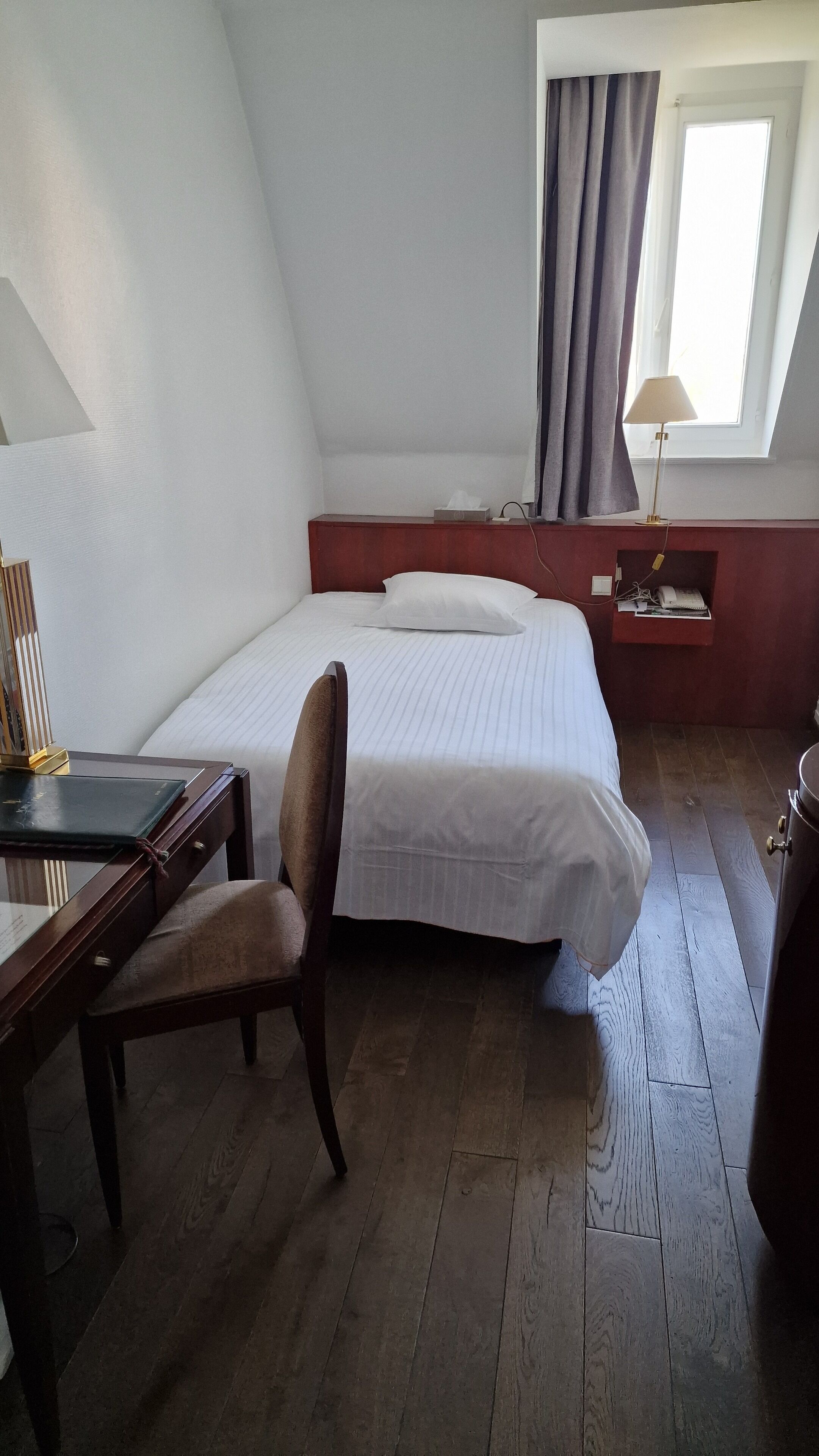 A room with a bed, a desk, a chair, a lamp, and a window with curtains.