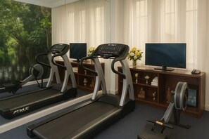 A room with three treadmills, a television, and a desk with a vase of flowers. - Hotel du Parc - Centre Ville (Mulhouse)