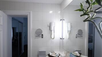A modern bathroom with white tiles, a large mirror, two round mirrors, a sink with toiletries, and a heating vent.