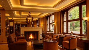 A warmly lit lounge area with a fireplace, leather sofas, and large windows offering a view of the outdoors. - Hotel du Parc - Centre Ville (Mulhouse)