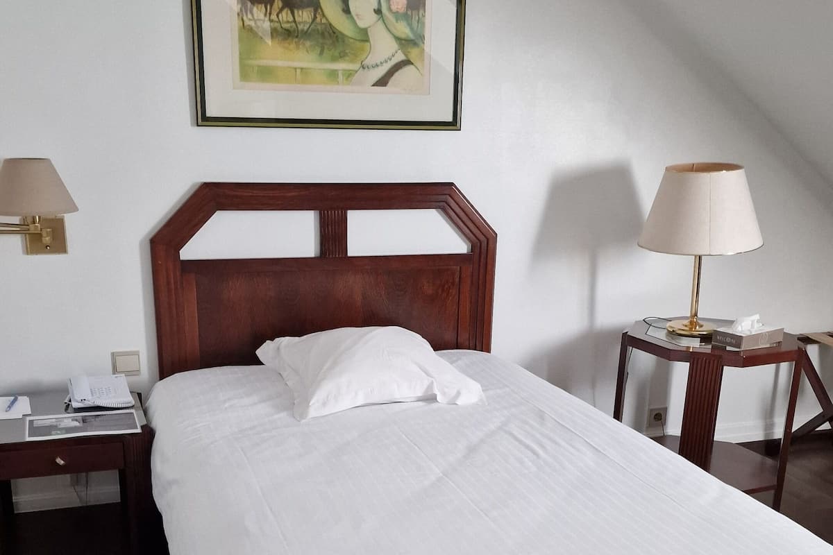 A neatly made bed in a room with a wooden headboard, a framed painting on the wall, and two bedside tables with lamps.