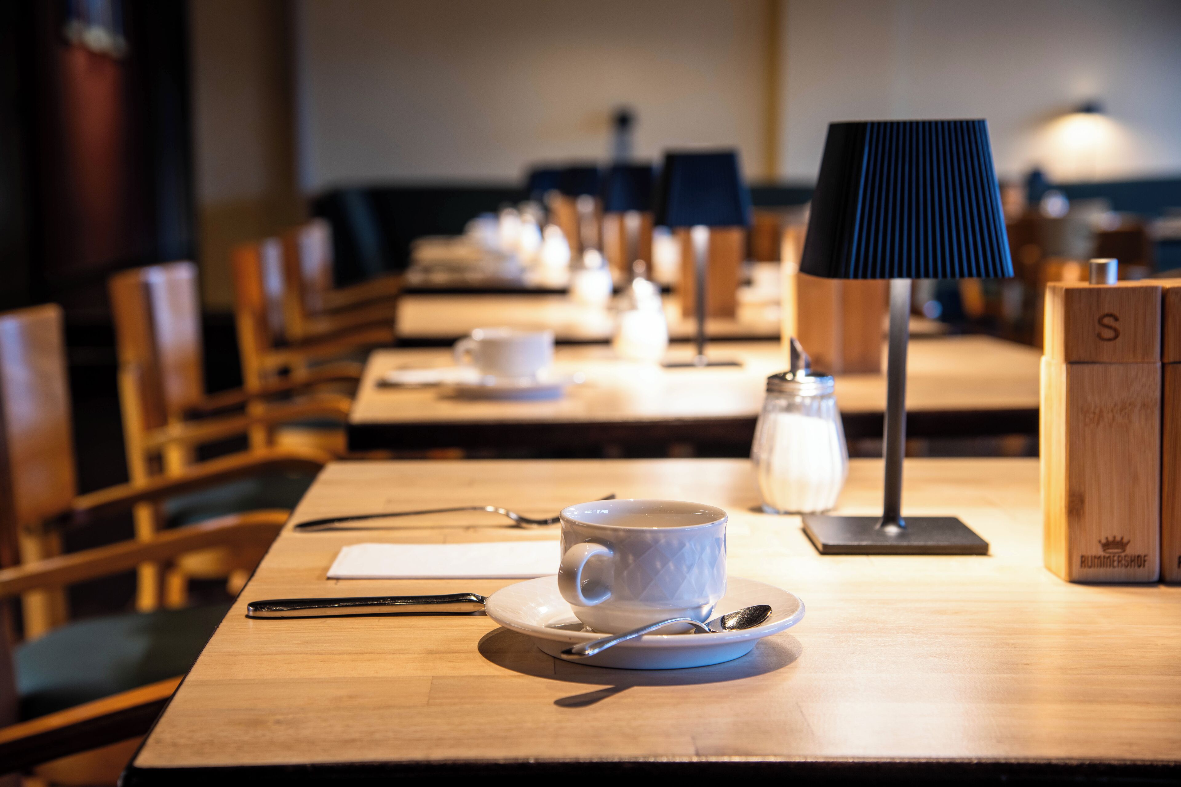 Un comedor con mesas dispuestas para una ceremonia de té, incluyendo tazas, platitos y cucharas.