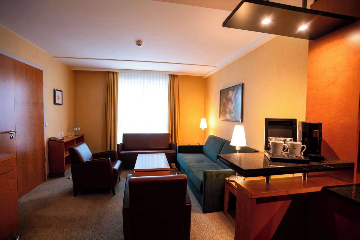 Een hotelkamer met een bank, fauteuils, een tafeltje, een koffieapparaat en een televisie.