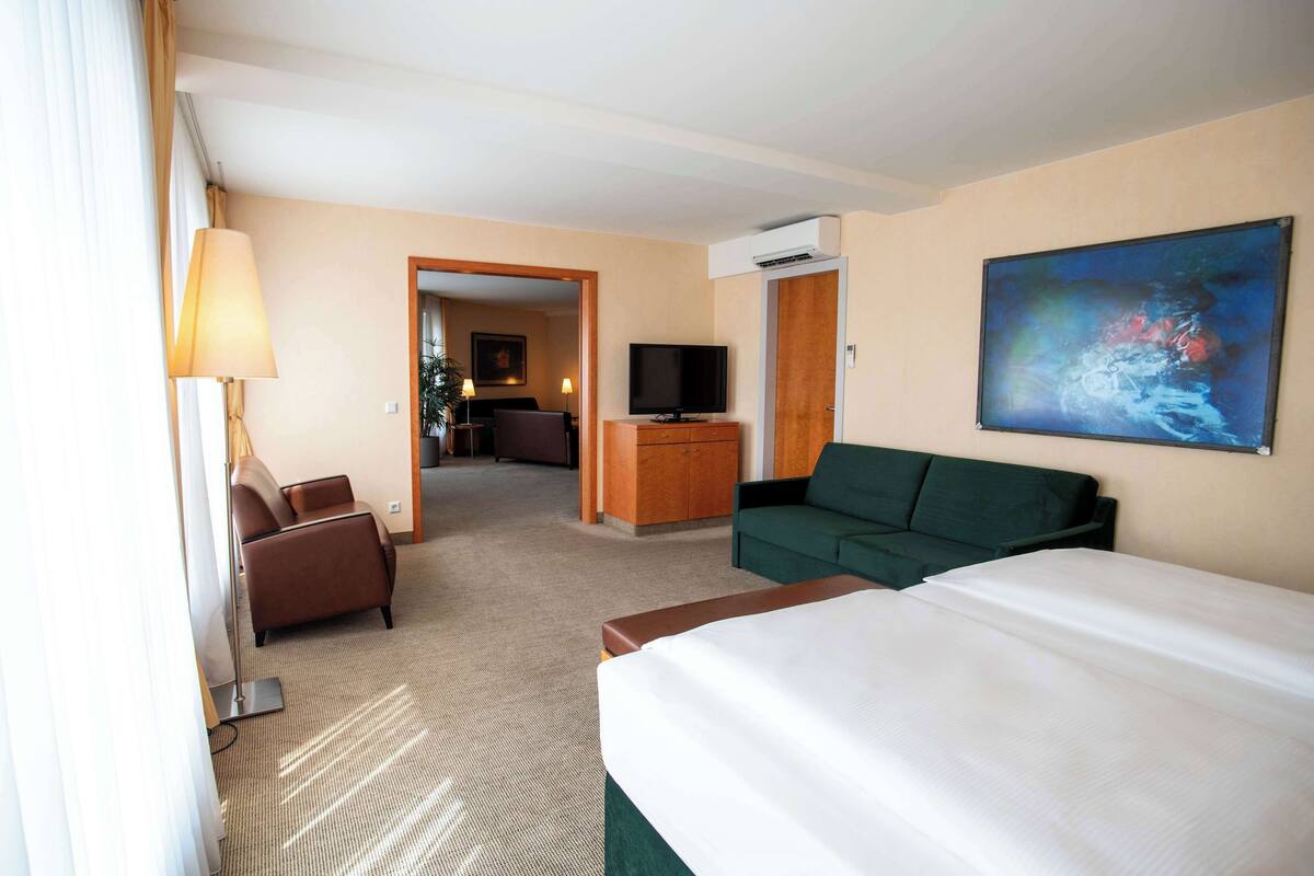Een hotelkamer met een groot bed, een groene bank, een televisie en een schilderij aan de muur.