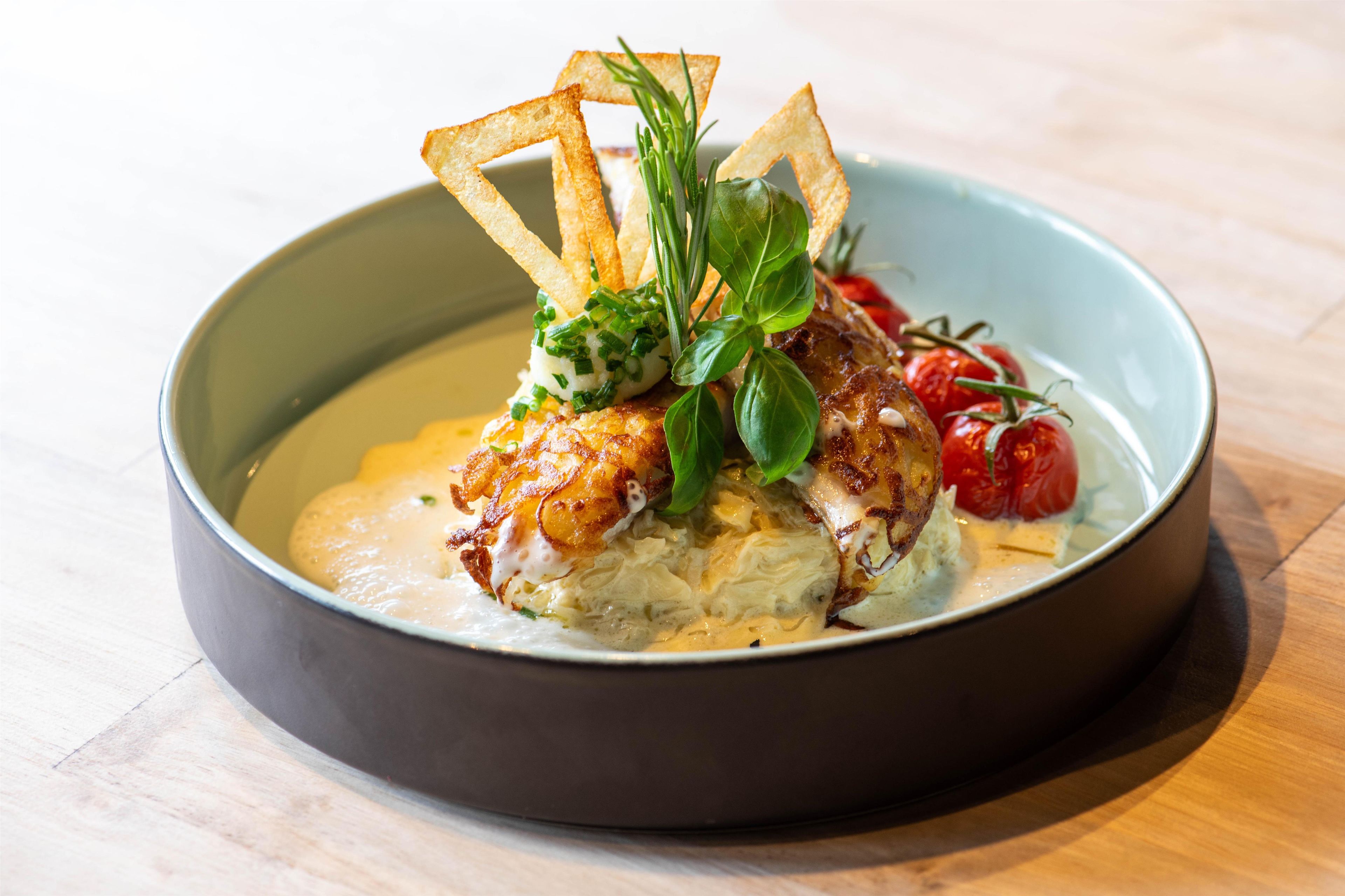 Un plato con base cremosa, coronado por un ingrediente dorado, adornado con hierbas verdes y un elemento crujiente.