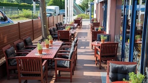 An outdoor patio area with wooden tables and chairs, potted plants, and a view of the street.