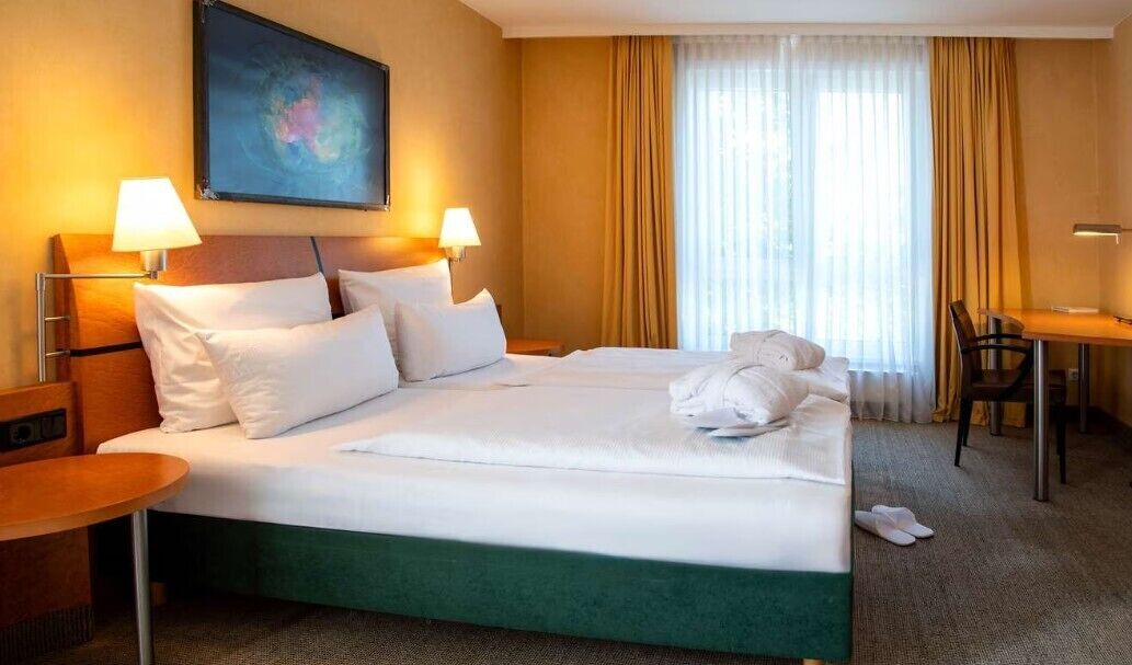 Een hotelkamer met een bed, twee bedlampjes, een bureau, een stoel en een schilderij aan de muur.