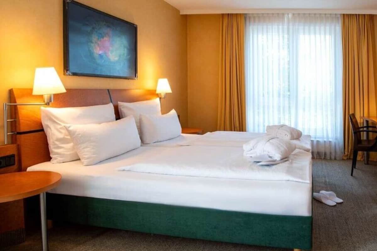 Een hotelkamer met een bed, twee bedlampjes, een bureau, een stoel en een schilderij aan de muur.
